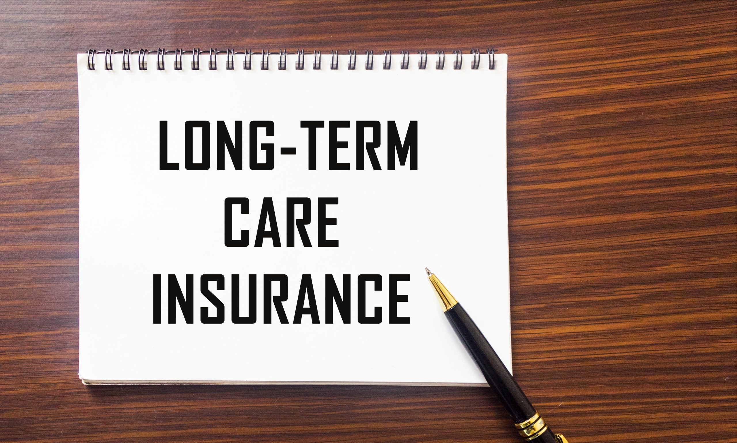 LONG TERM CARE INSURANCE information close-up written on a notepad and a wooden background. Medical concept